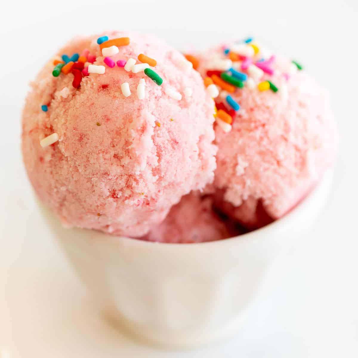 A white bowl of strawberry snow ice cream topped with rainbow sprinkles.