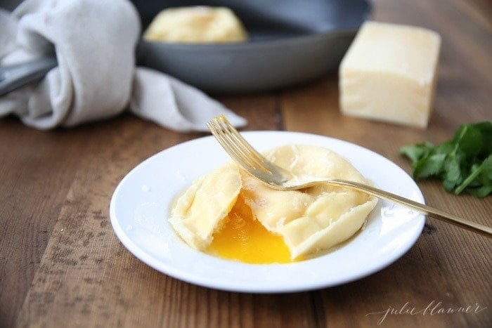 Egg ravioli on a white plate cut in half with a fork