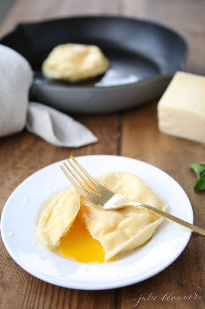 Egg ravioli on a white plate with a fork with the egg yolk oozing out