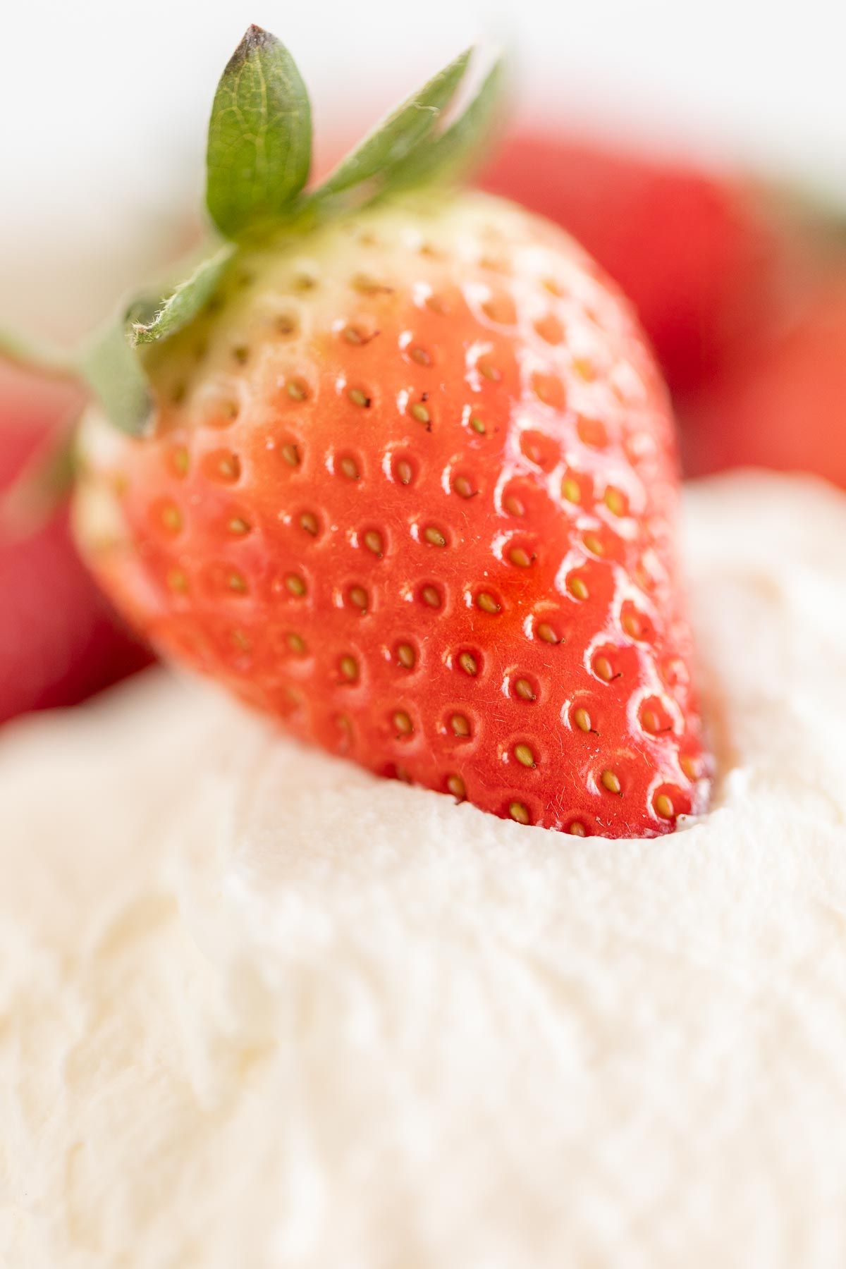 A strawberry resting on a bowl of mascarpone dip.