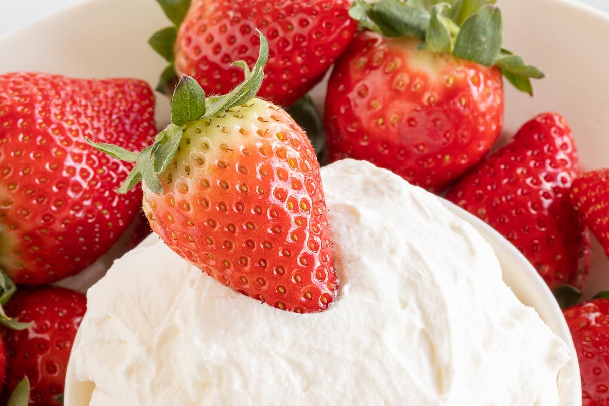 A strawberry resting on a bowl of mascarpone dip.