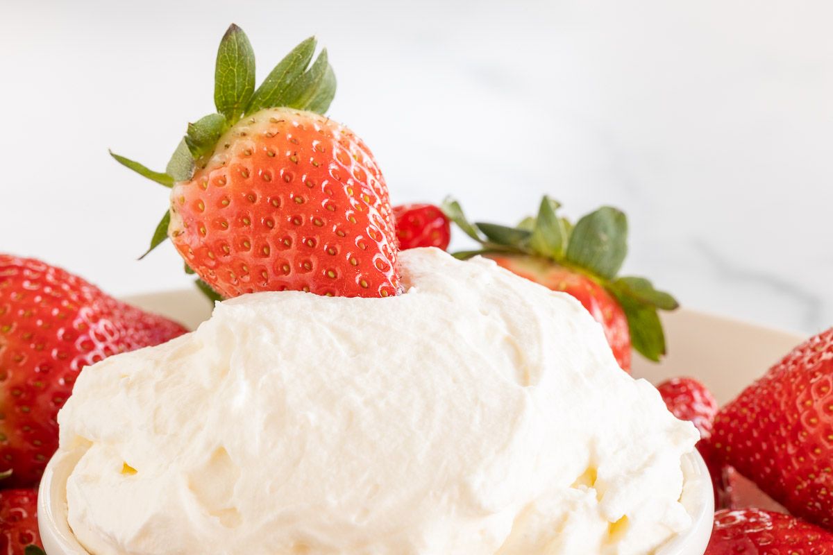 A strawberry resting on a bowl of mascarpone dip.