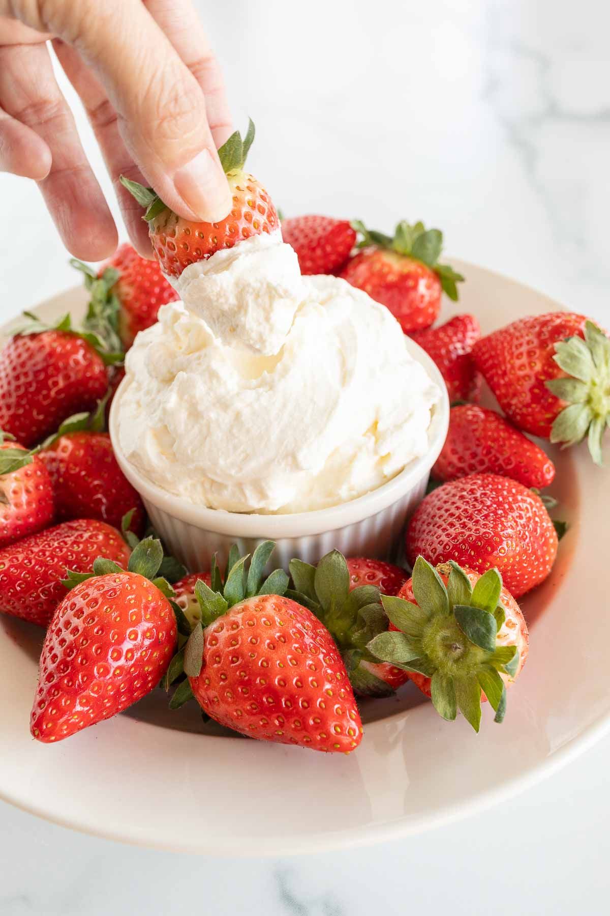 A white plate full of strawberries and a bowl of mascarpone dip in the center.