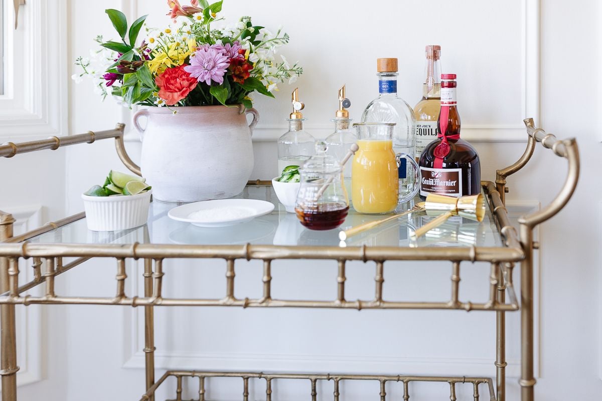 Ingredients for a margarita cocktail set up on a gold bar cart
