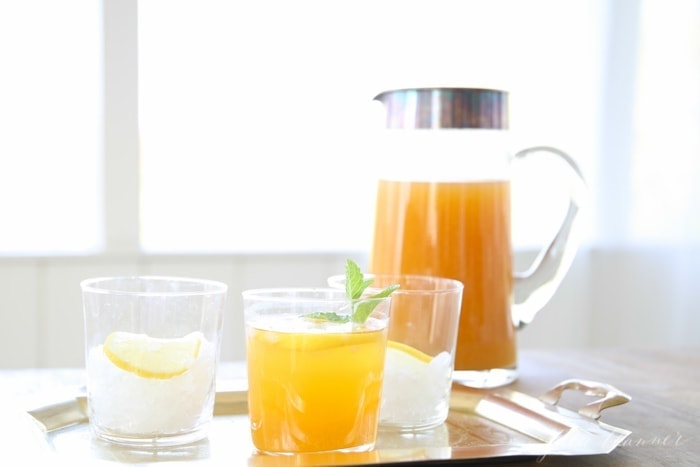 Three glasses on a serving tray, one filled with spiked peach sweet tea