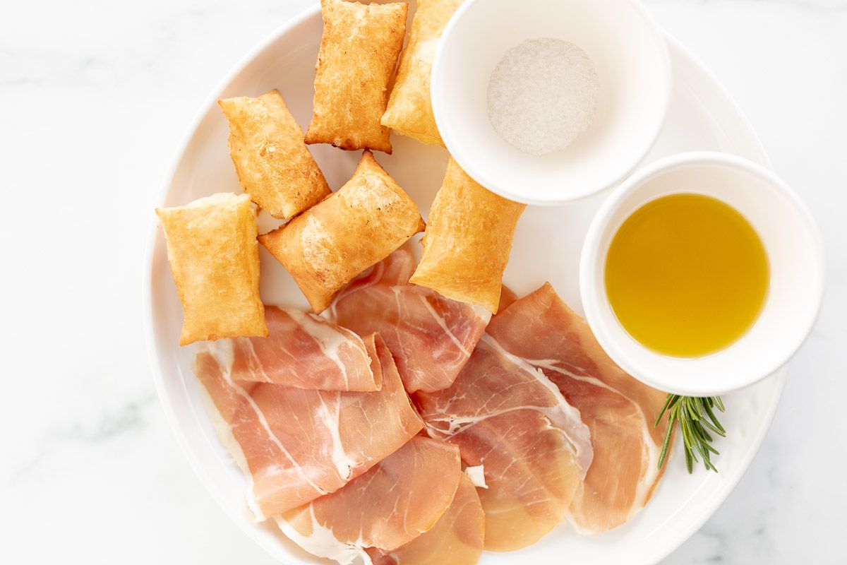 Gnocco fritto on a white plate with bowls of olive oil and sea salt to the side