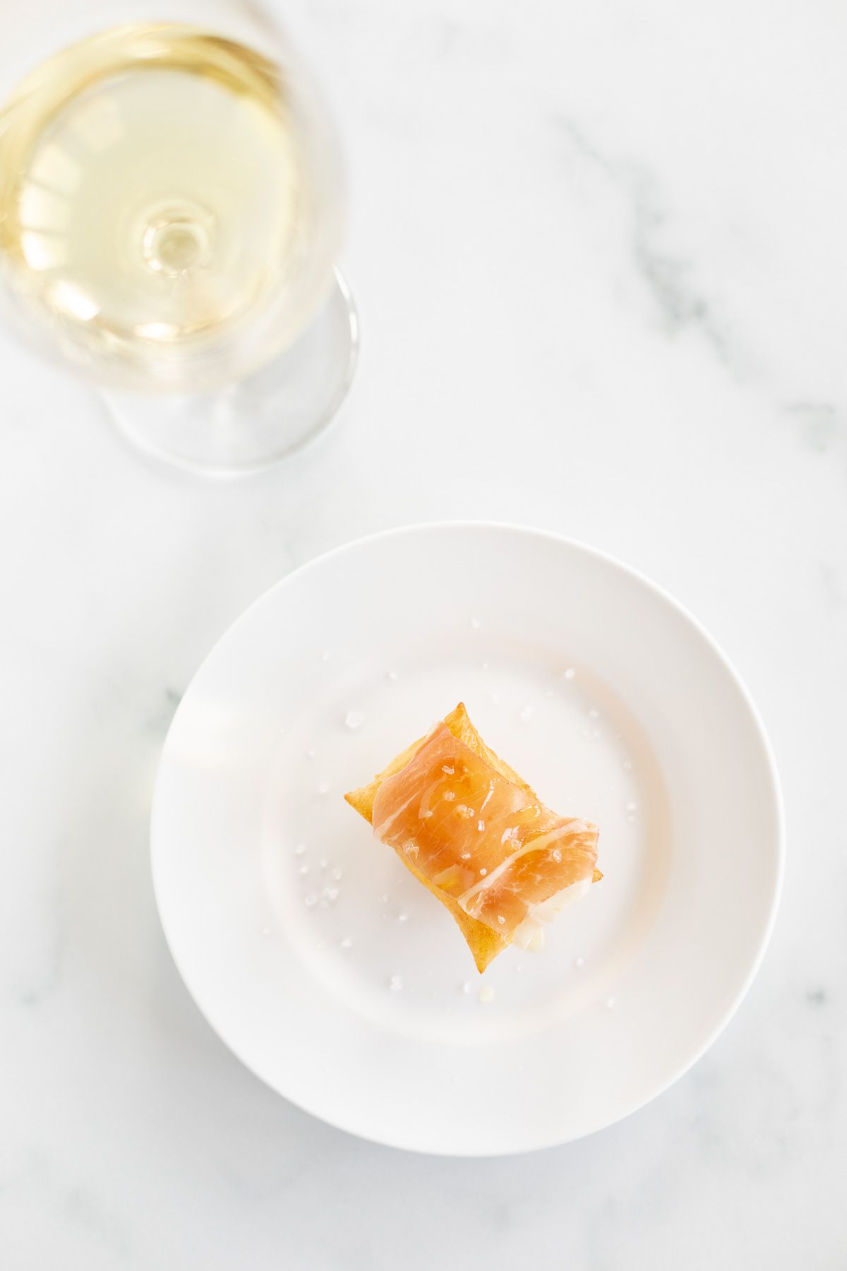 A white plate with a single gnocco fritto and a glass of wine to the side