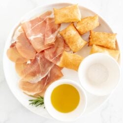 Gnocco fritto on a white plate with bowls of olive oil and sea salt to the side