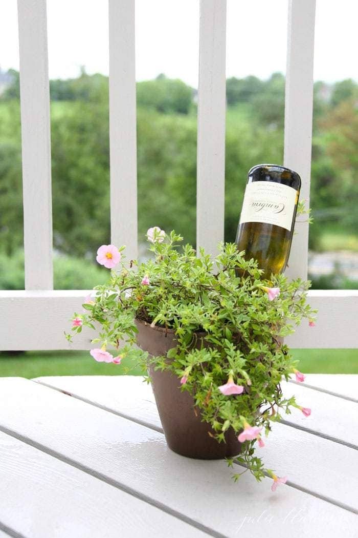 A vase of flowers on a white porch with a wine bottle inside. 