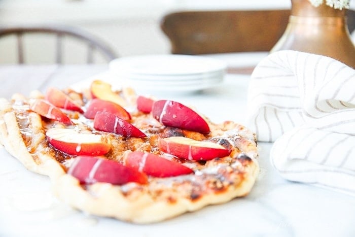 Dessert pizza topped with sliced peaches on a white tablecloth