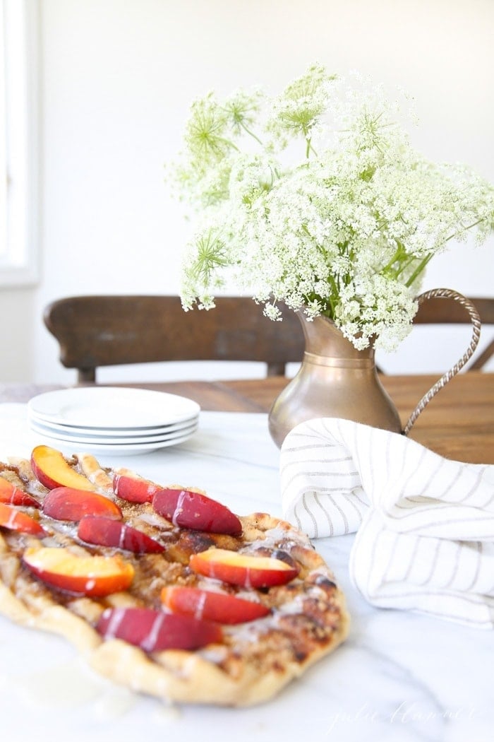 Dessert pizza topped with sliced peaches on a white tablecloth