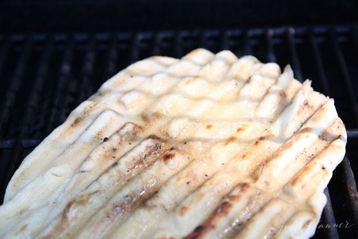 Pizza dough spread out on an outdoor grill, topped with cinnamon and brown sugar