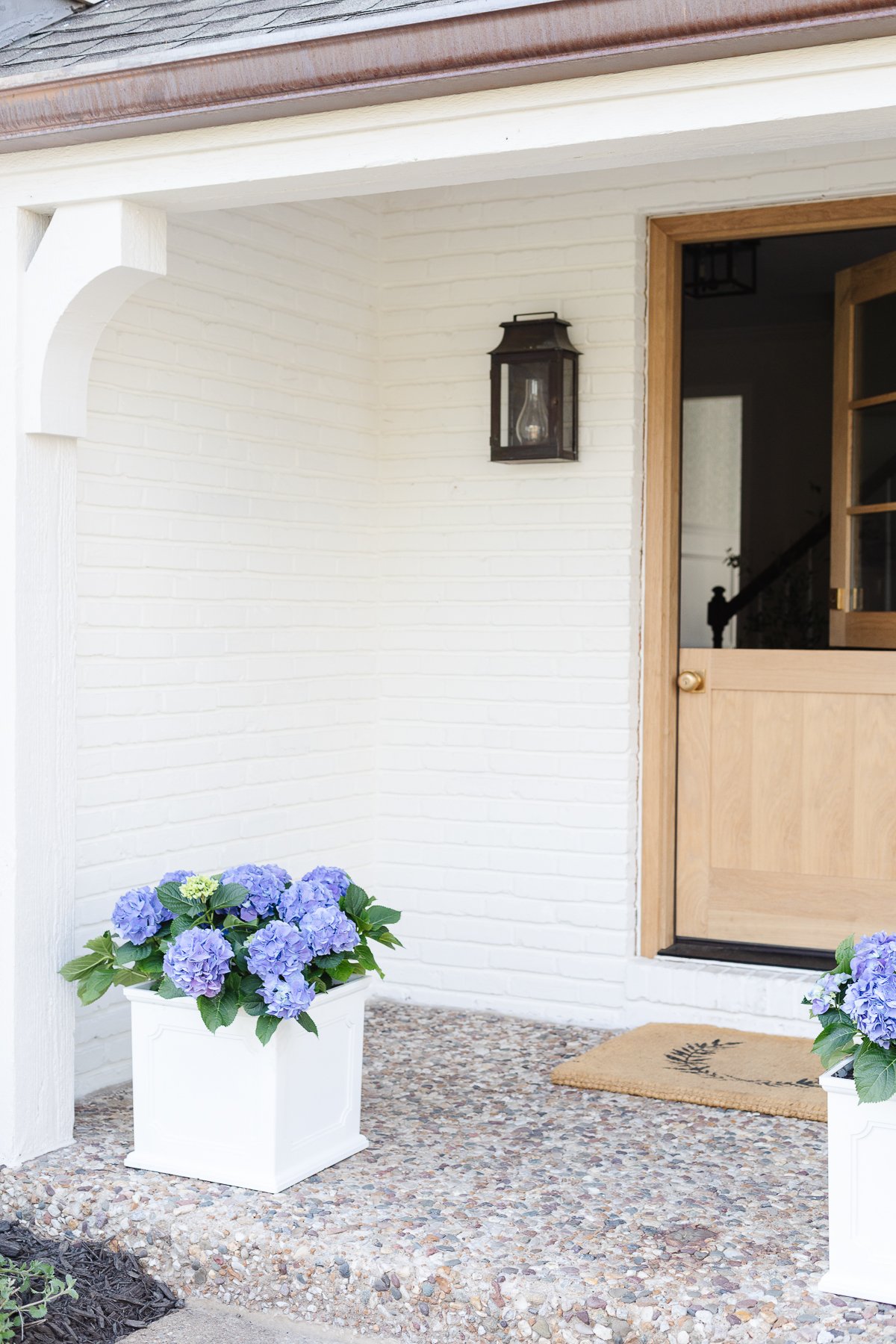 A white front porch planter with blue hydrangea on a small covered front porch.