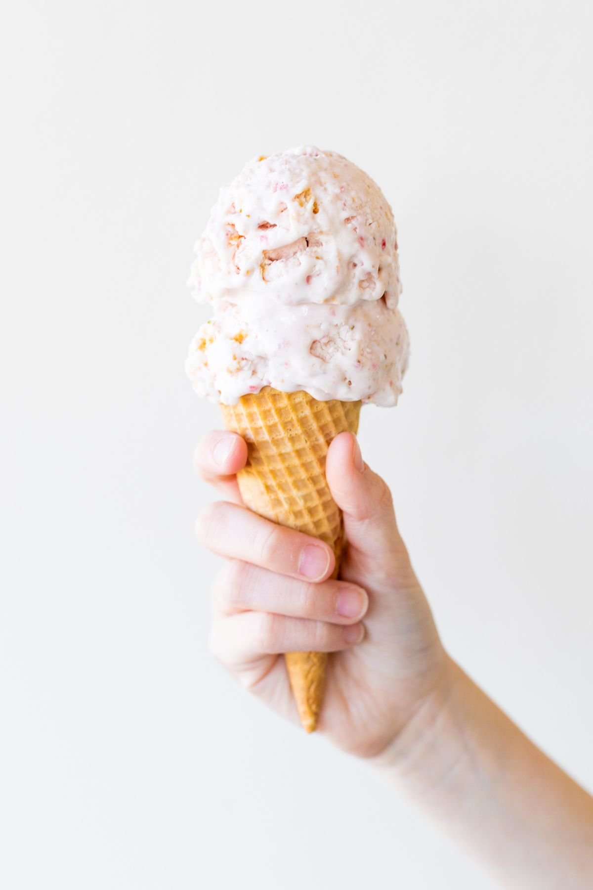 A hand holding a cone of strawberry cheesecake ice cream.