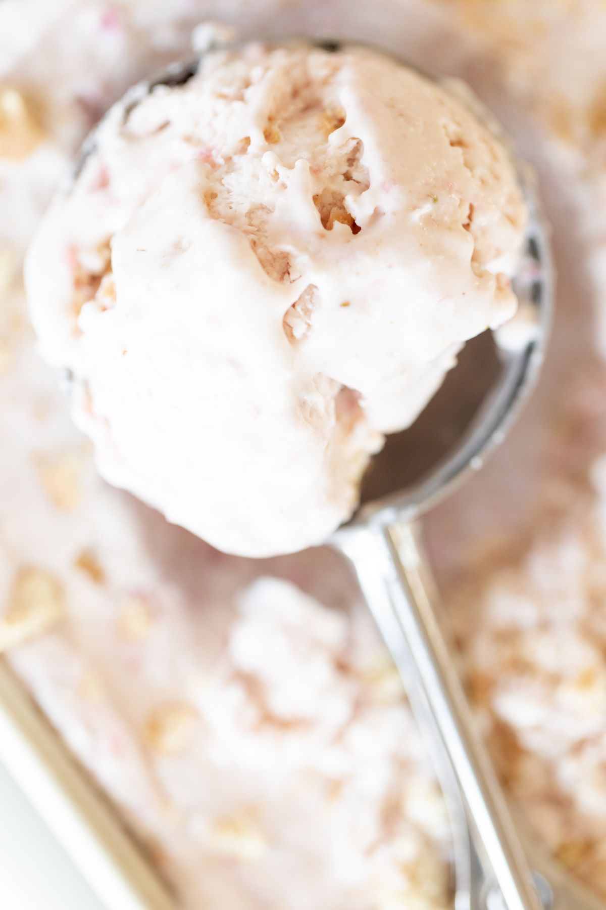 A scoop pulling out a serving of strawberry cheesecake ice cream.