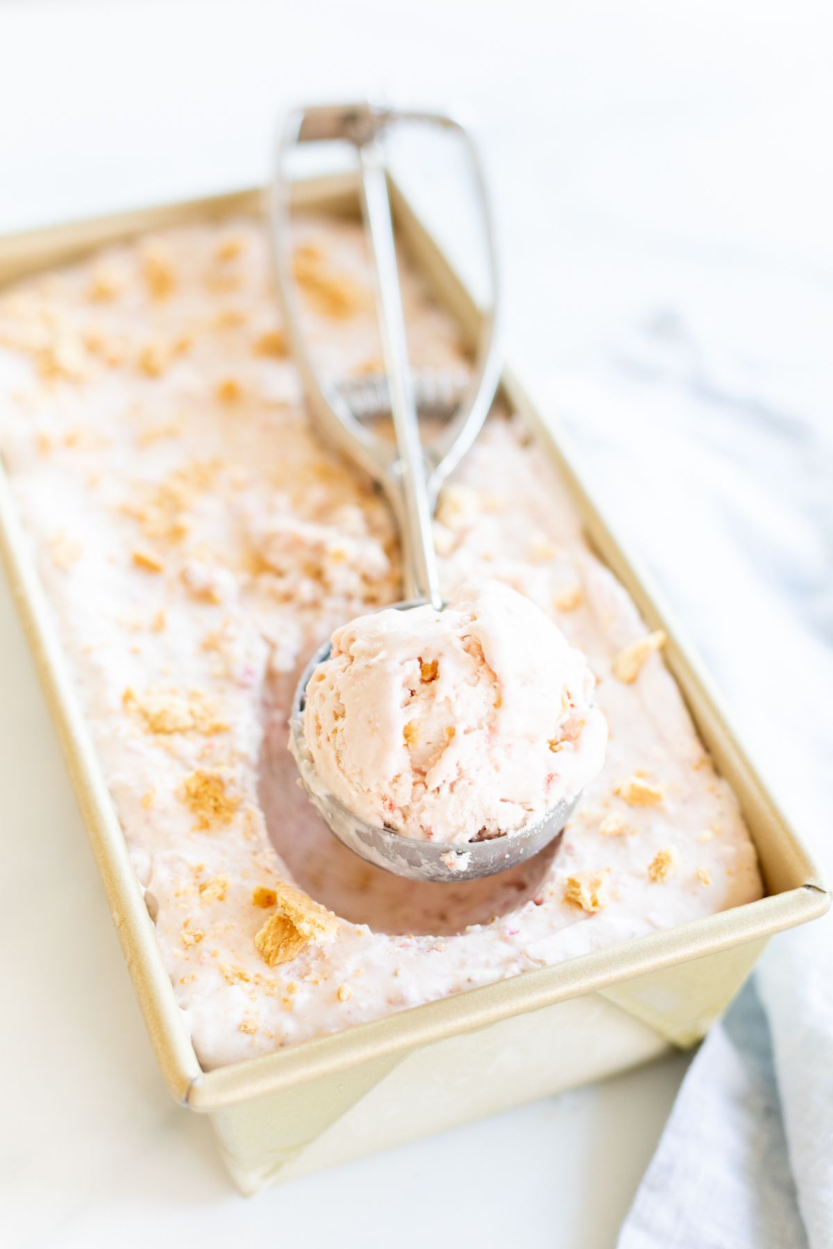 A scoop pulling out a serving of strawberry cheesecake ice cream.