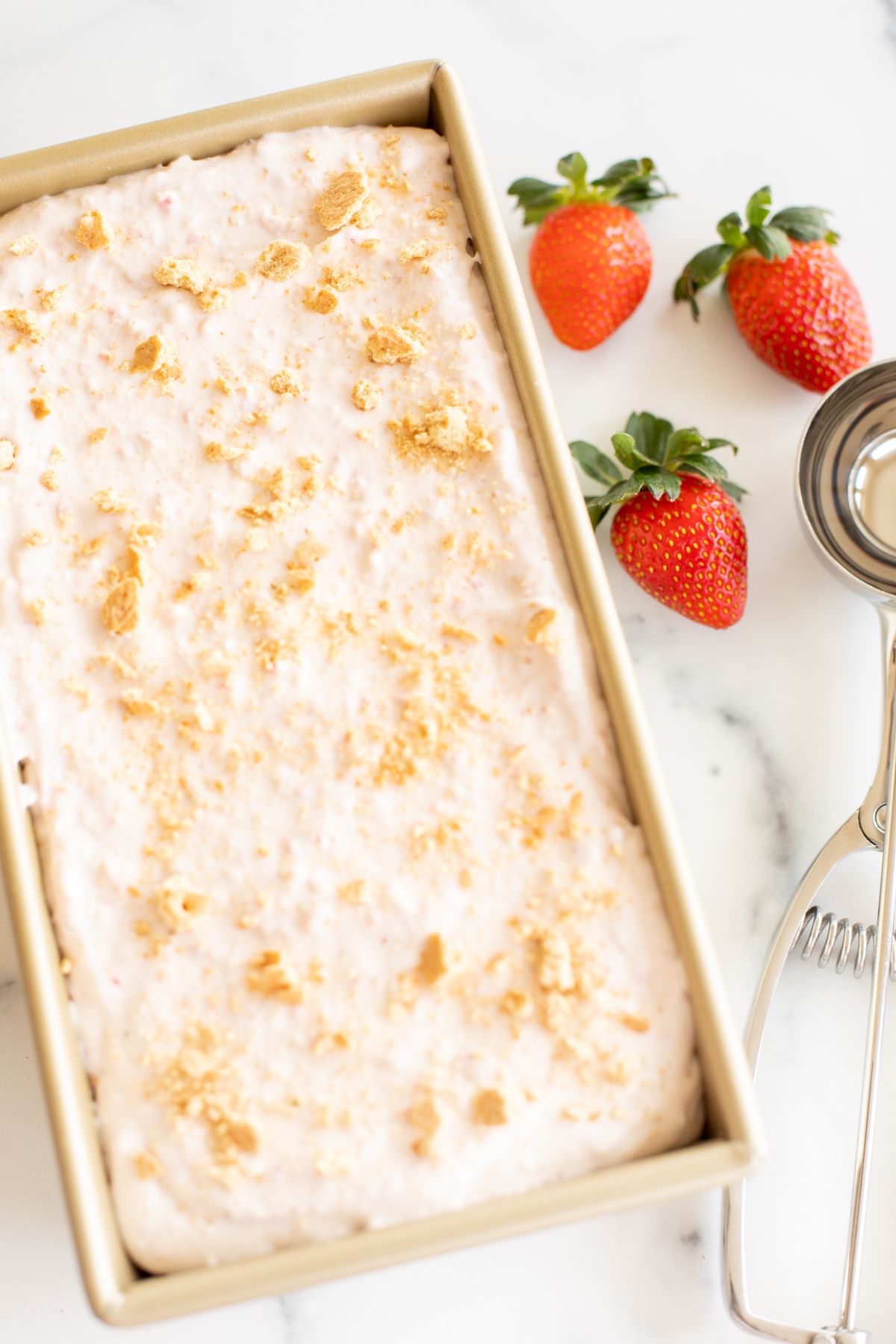 A gold loaf pan filled with creamy homemade strawberry cheesecake ice cream.