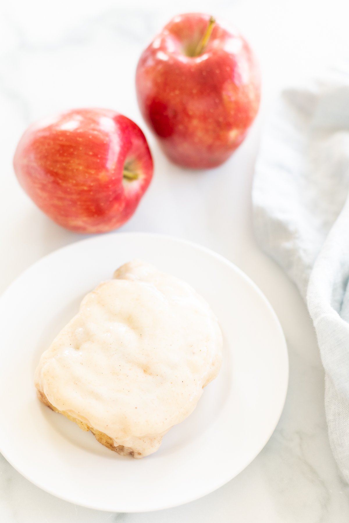 A white plate with apple cinnamon rolls and icing on it.