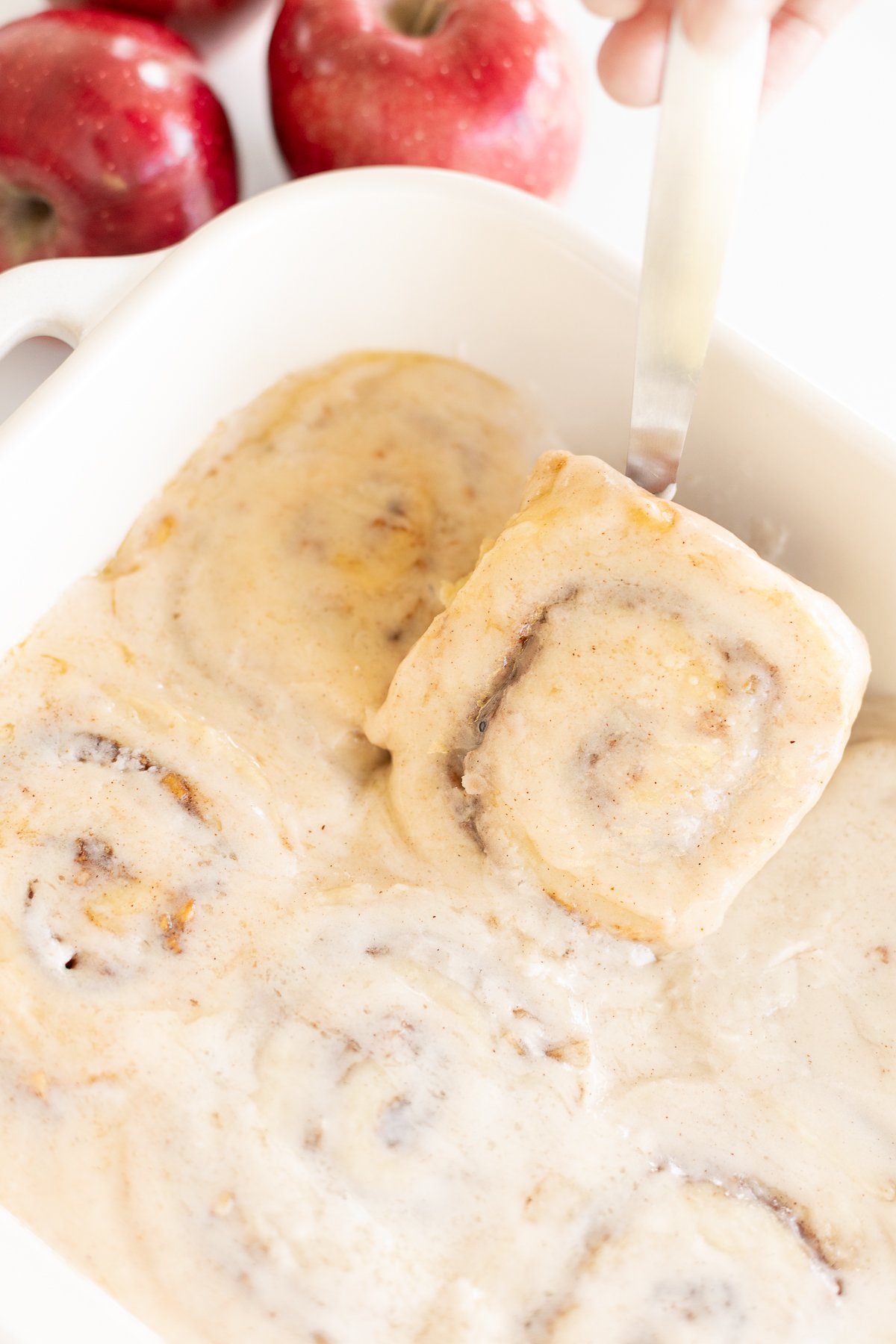 A person delicately scooping apple cinnamon rolls out of a baking dish.