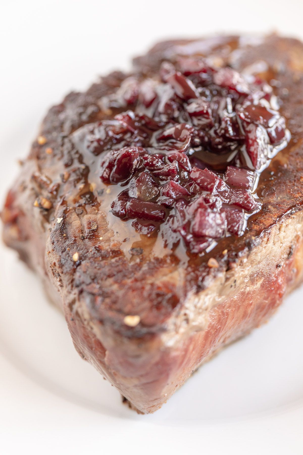 A steak on a white plate, topped with red wine sauce