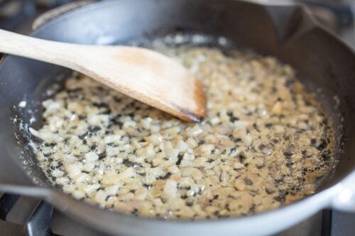 Shallots cooking in a cast iron pan, wooden spoon to the side