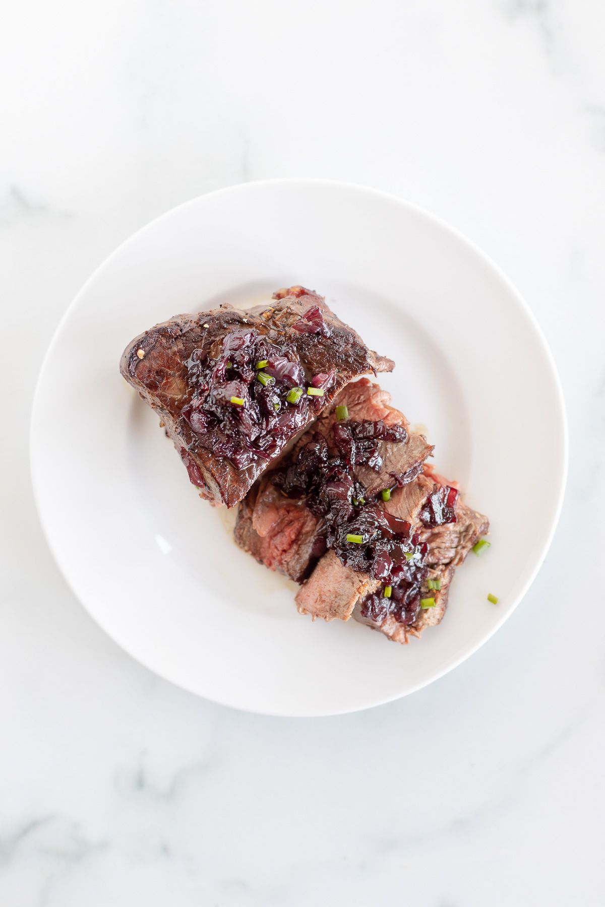 A white plate with a steak topped with red wine sauce for steak.