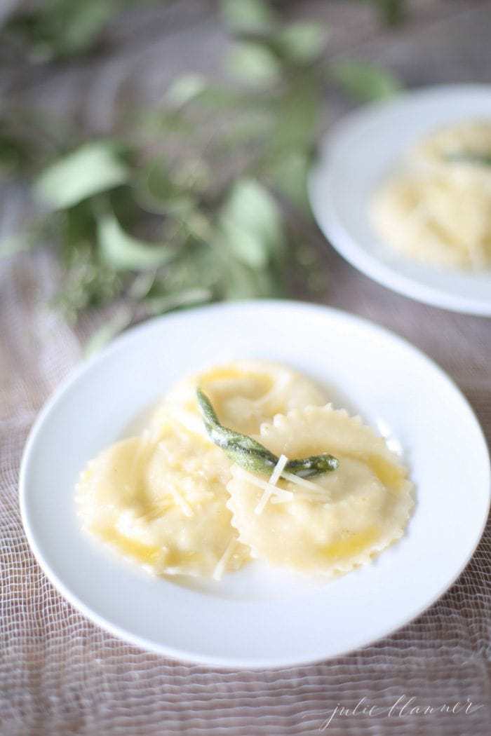 wonton ravioli in butter sage sauce on a white plate with sage leaves in background