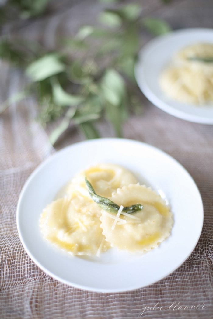 wonton ravioli in butter sage sauce on a white plate with sage leaves in background