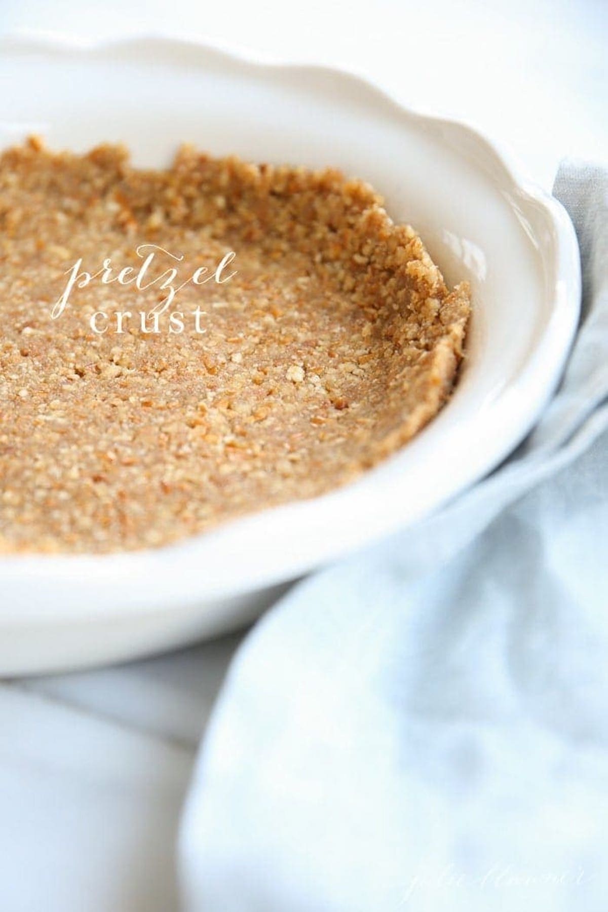 A pretzel pie crust in a white pie dish, blue linen towel to the side.