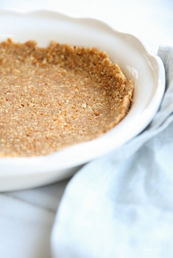 A pretzel pie crust in a white pie dish, blue linen towel to the side.