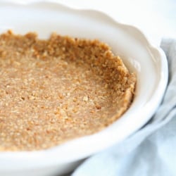 A pretzel pie crust in a white pie dish, blue linen towel to the side.