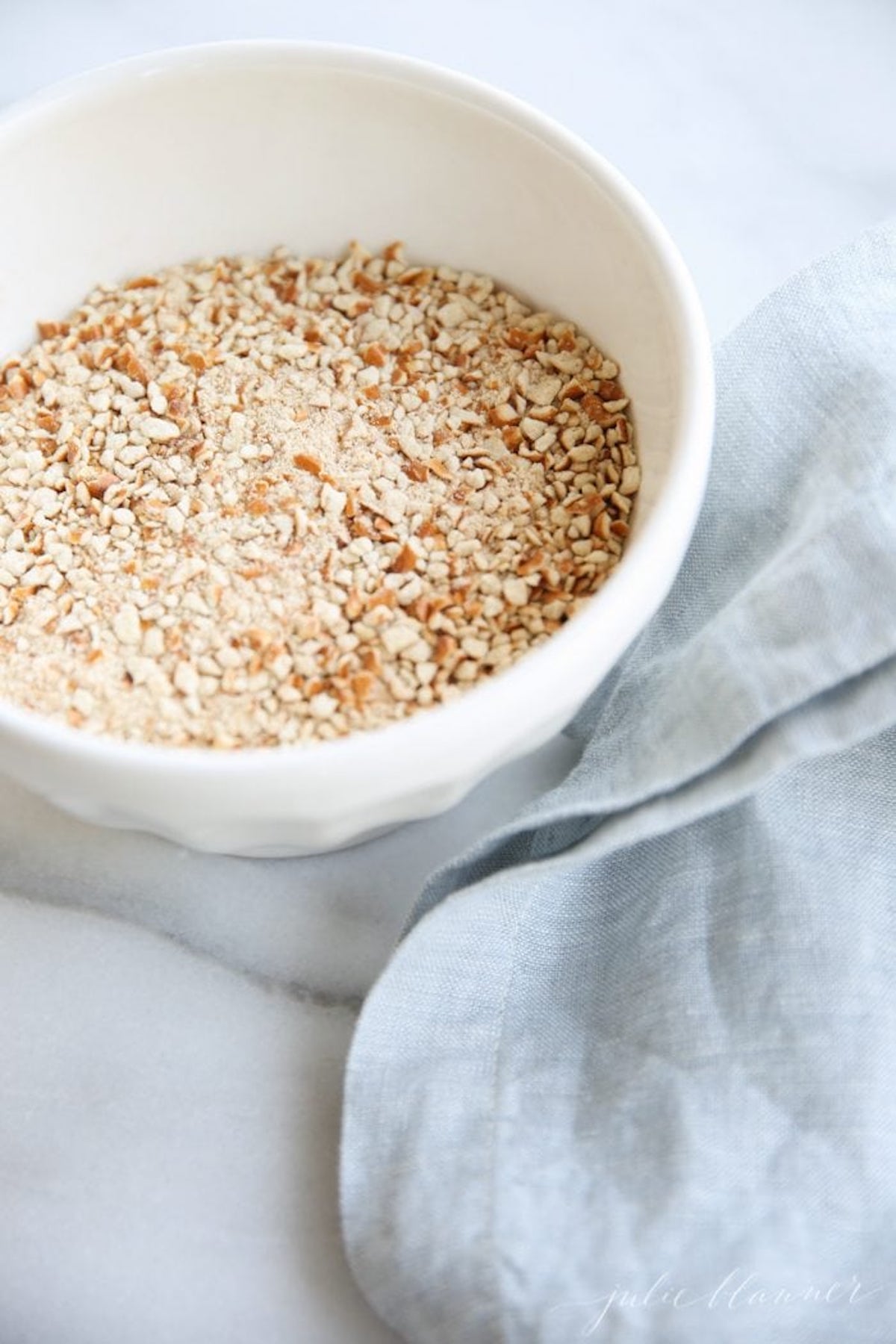 Crushed pretzels in a white bowl with a blue towel to the side.