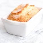 A loaf of freshly baked sweet bread in a white ceramic baking dish, placed on a light blue cloth.