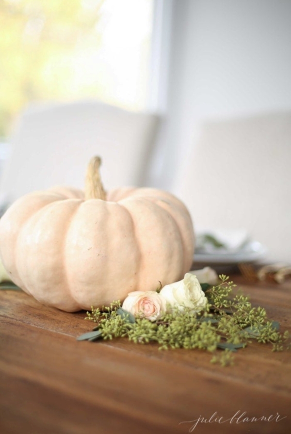 A Thanksgiving centerpiece set with a white pumpkin and fresh flowers below.