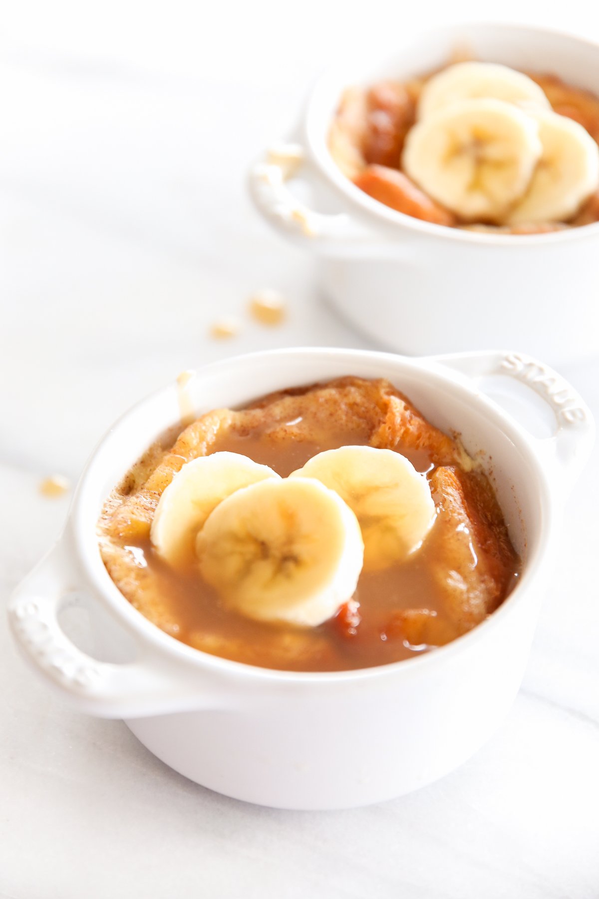 bread pudding in an individual, white baking dishes, topped with sliced bananas.