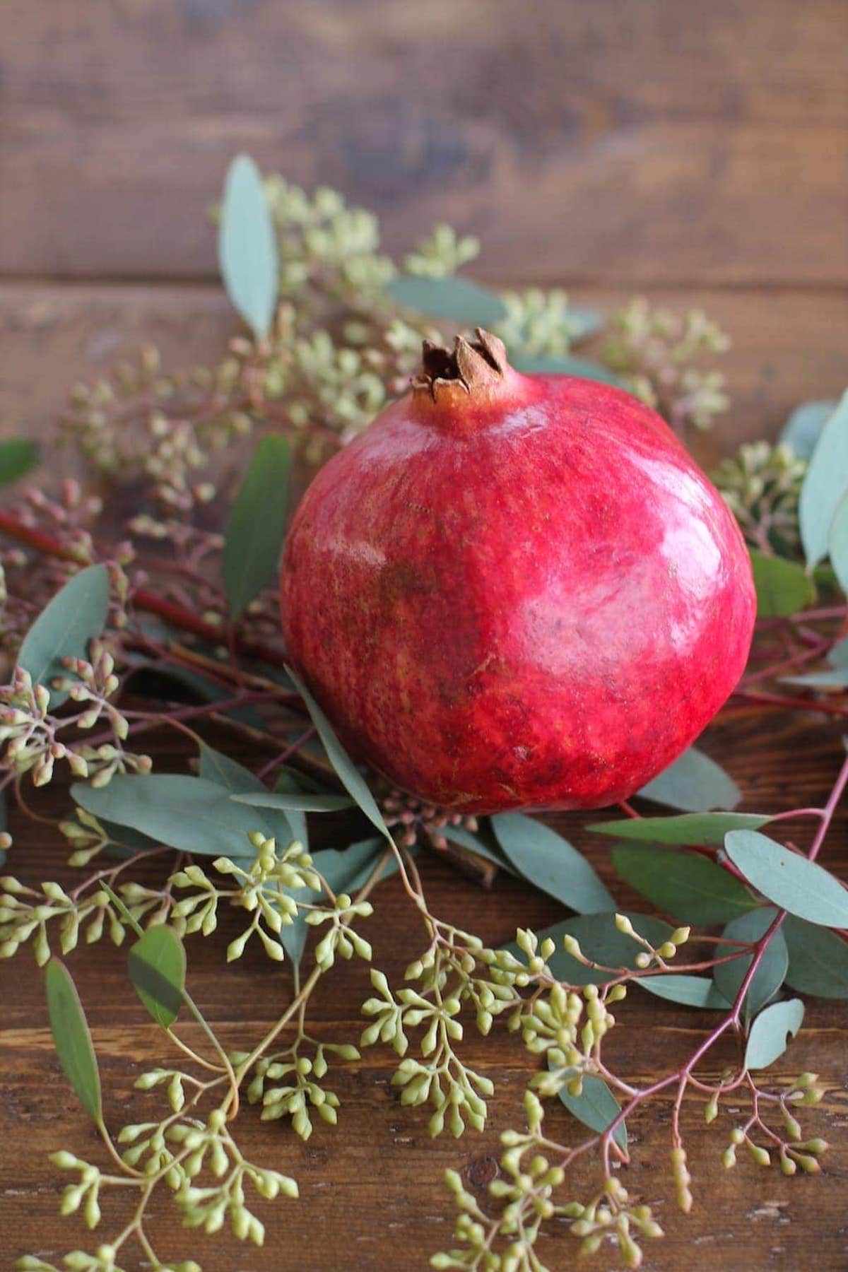 Christmas candle centerpiece featuring pomegranate and eucalyptus leaves on a wooden table.
