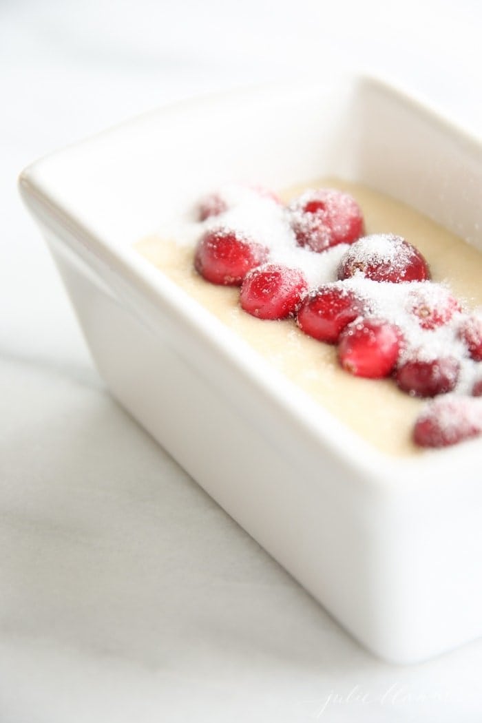 Quick bread batter topped with whole fresh cranberries and sugar in a small white loaf pan.