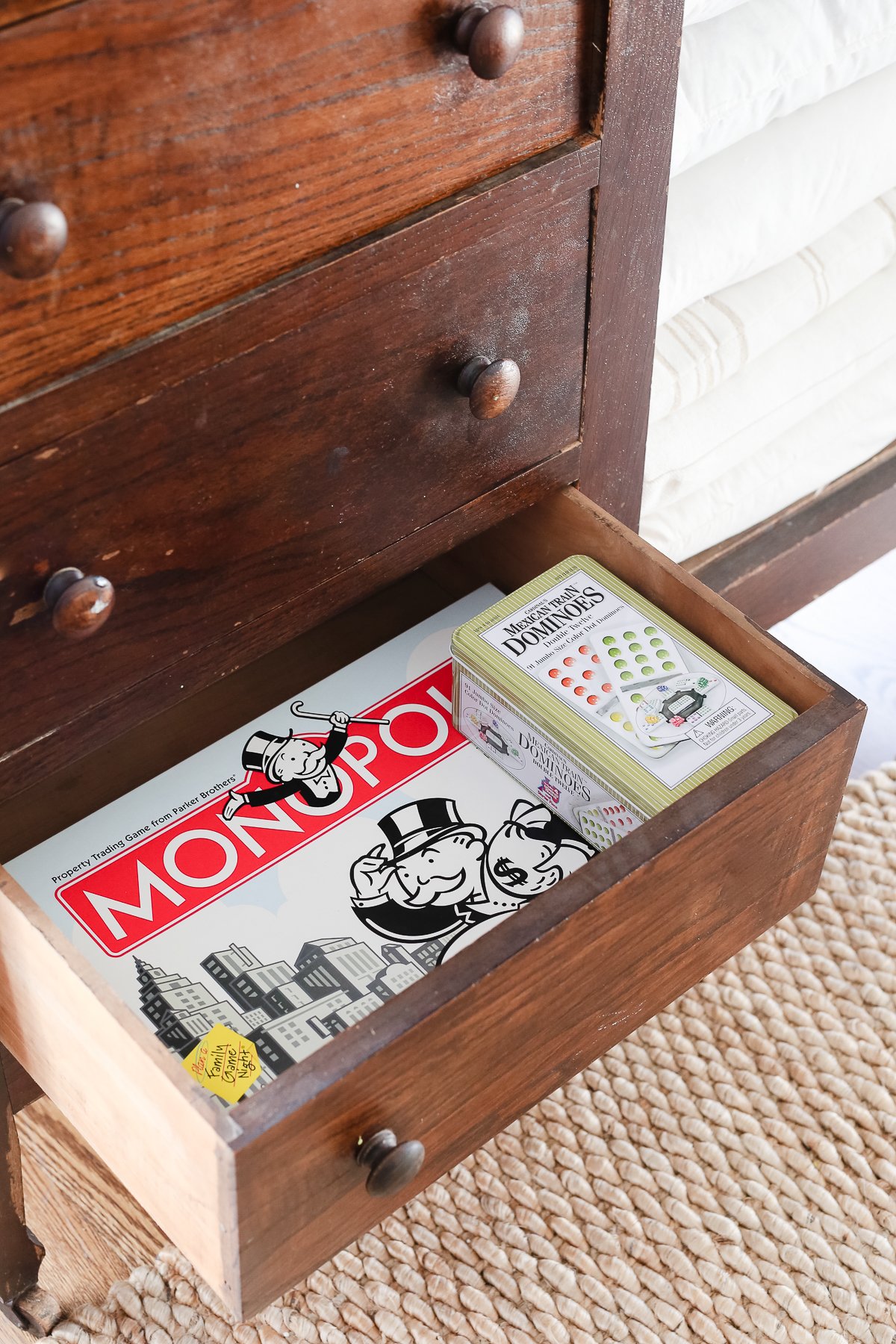 A dark wood linen cabinet in a family room space, with the drawers opened to reveal the interior storage.