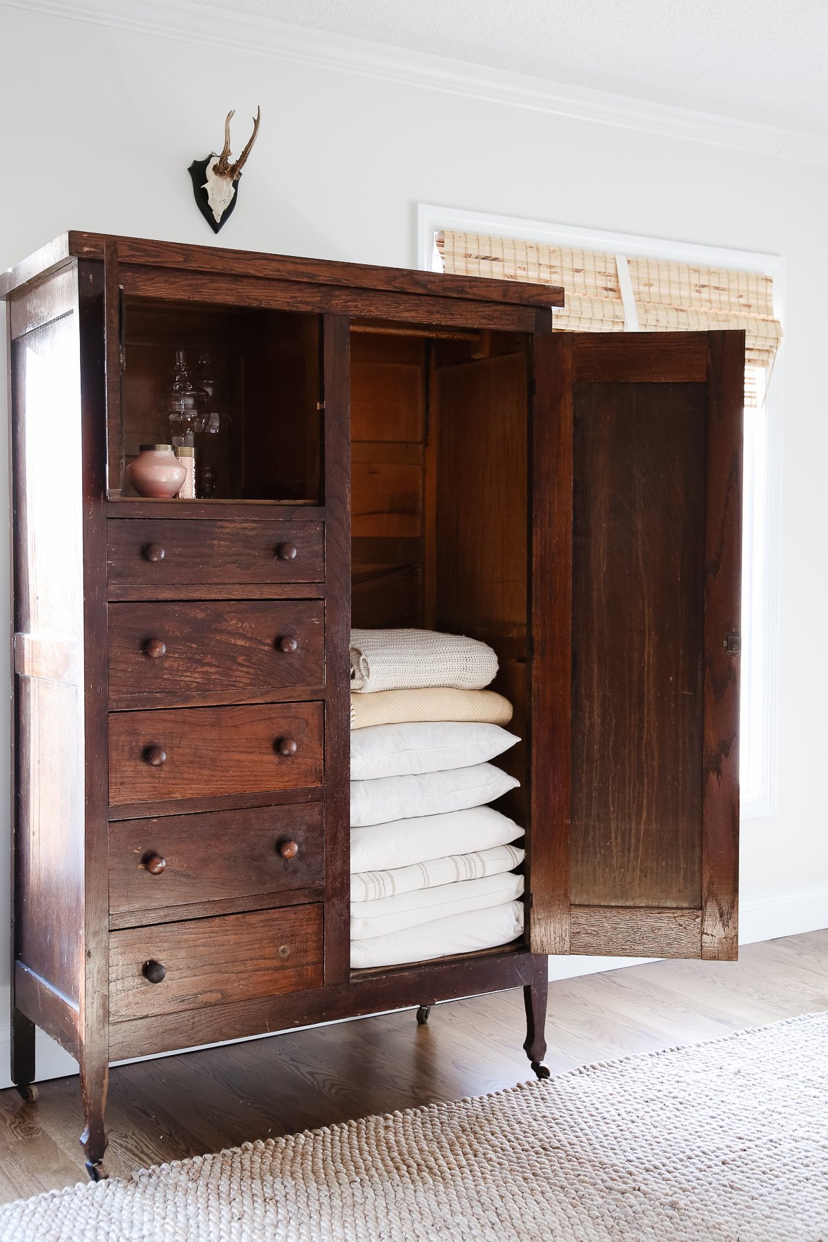 A dark wood linen cabinet in a family room space, with the door opened to reveal the interior storage.