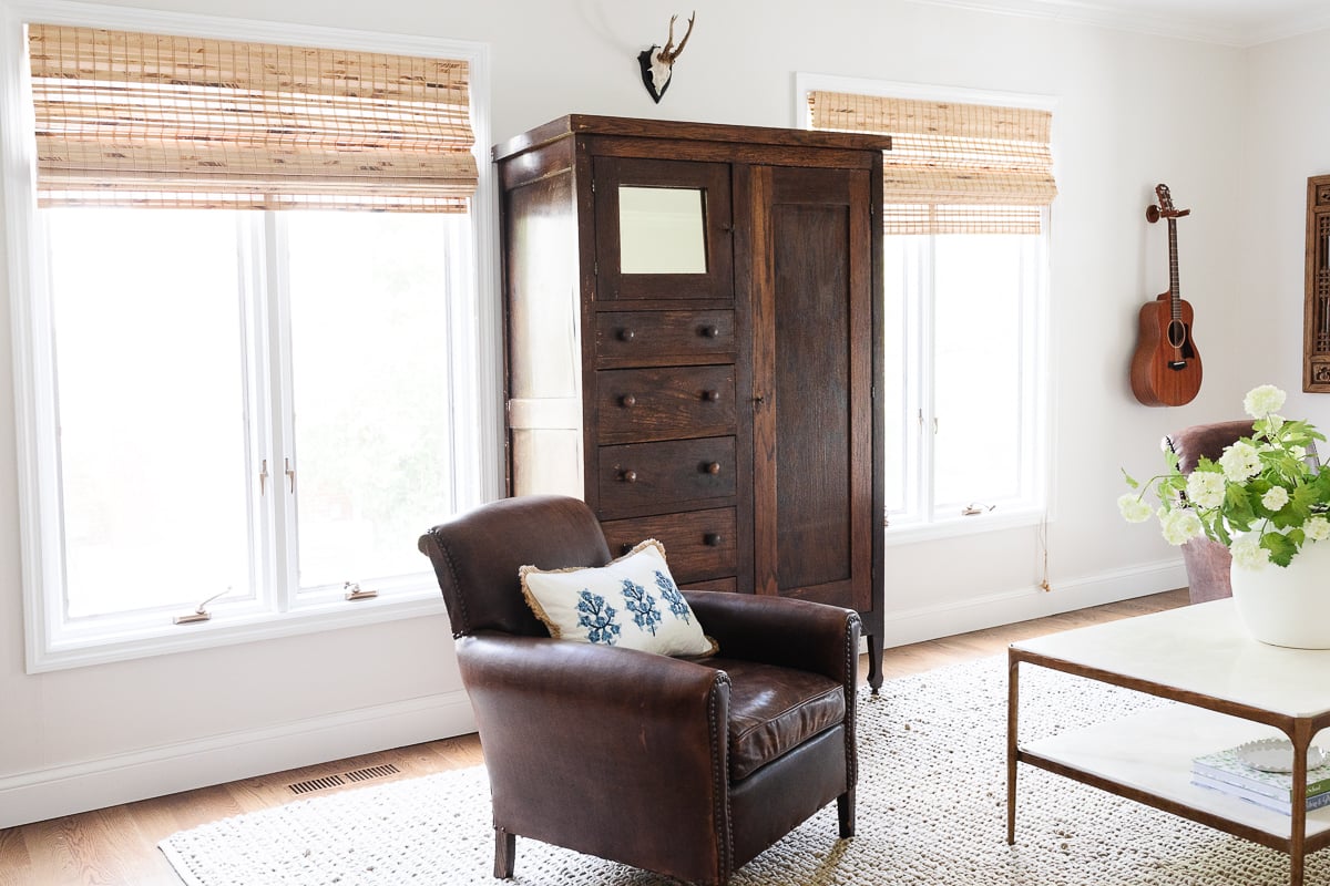 A white living room with a leather chair and a dark wood linen cabinet.