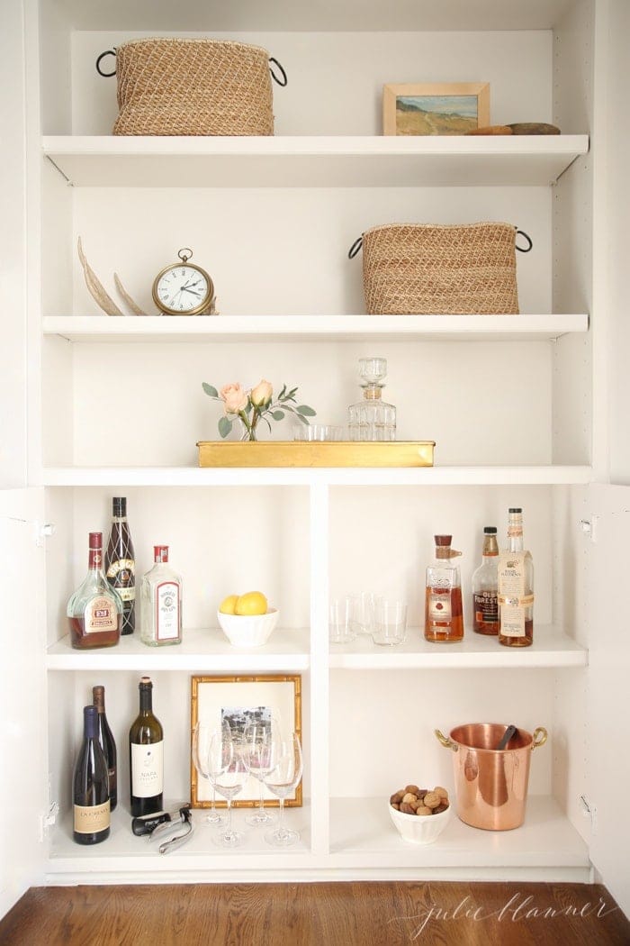 A white built in cabinet and book case in a living room, converted into a hidden bar area.