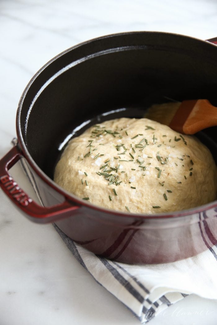 artisan bread dough in a brown dutch oven with pastry brush