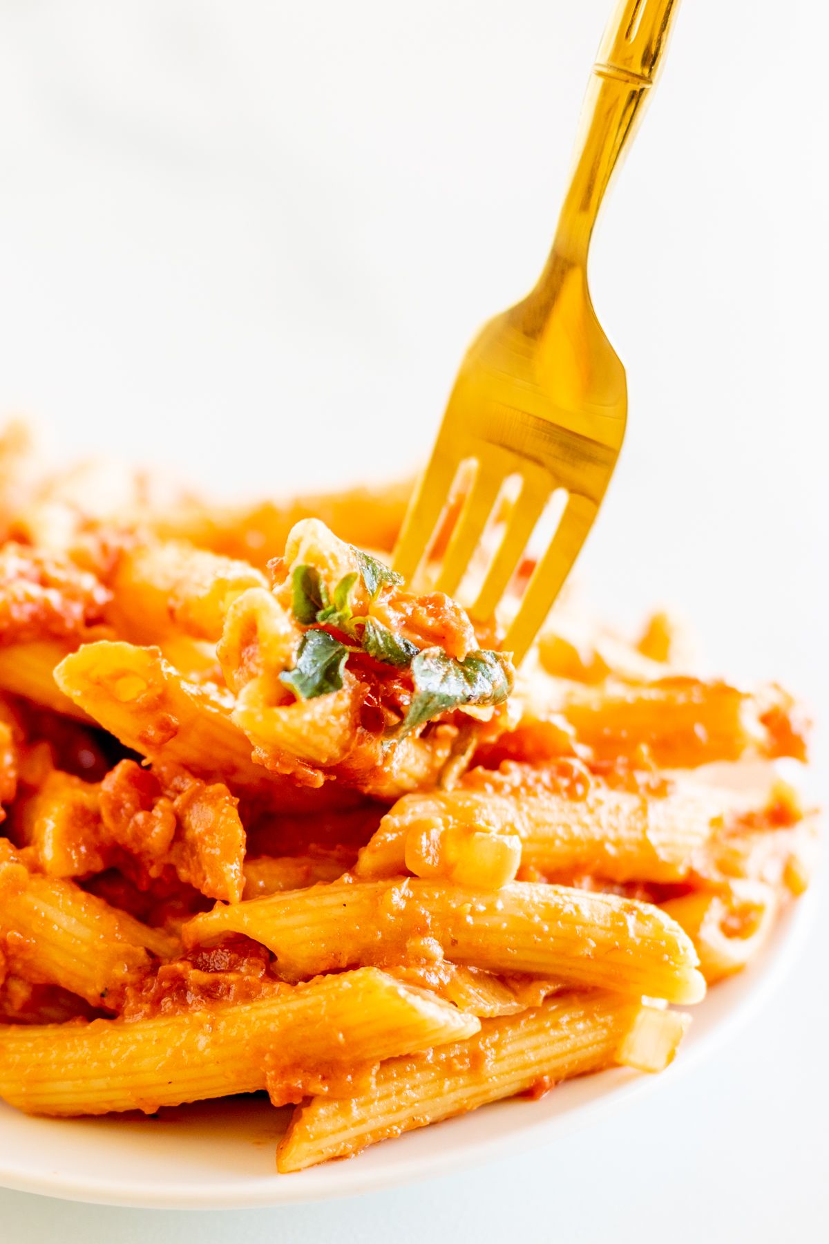 Penne alla vodka on a white plate with a gold fork.