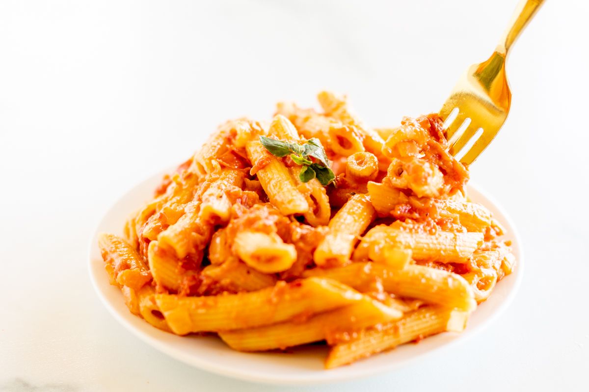 Penne alla vodka on a white plate with a gold fork.