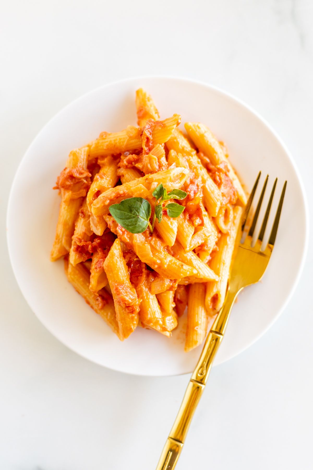 Penne alla vodka on a white plate with a gold fork.