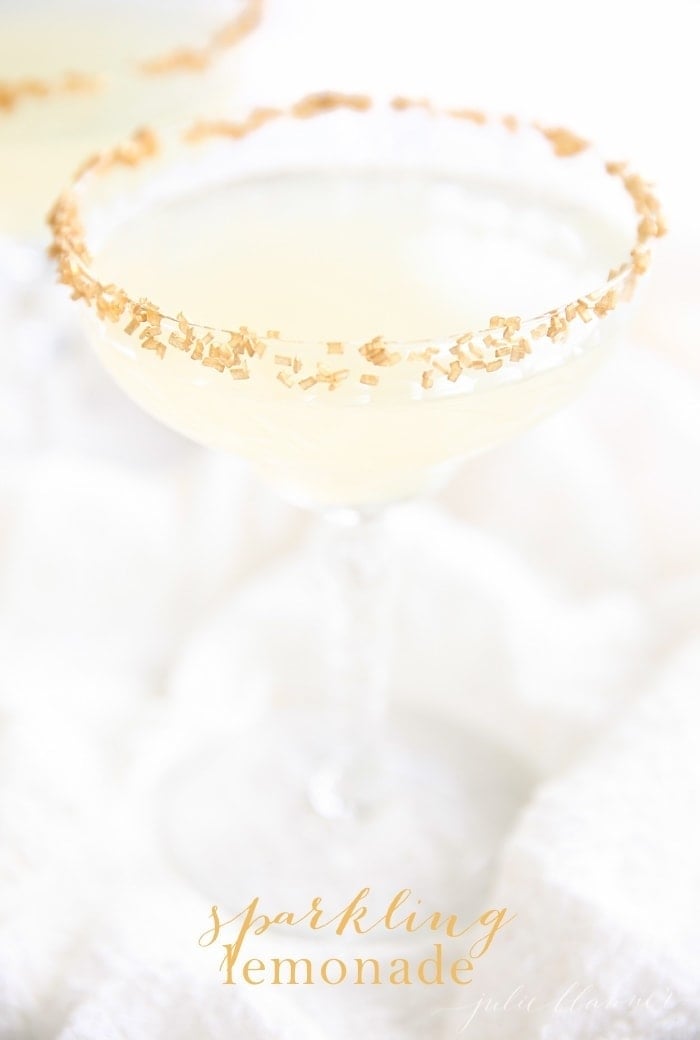 A sparkling lemonade cocktail with a gold rim, white background