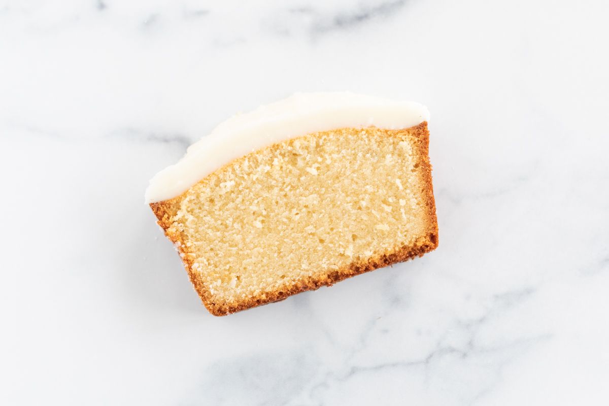 A slice of pound cake on a marble countertop, topped with glaze.