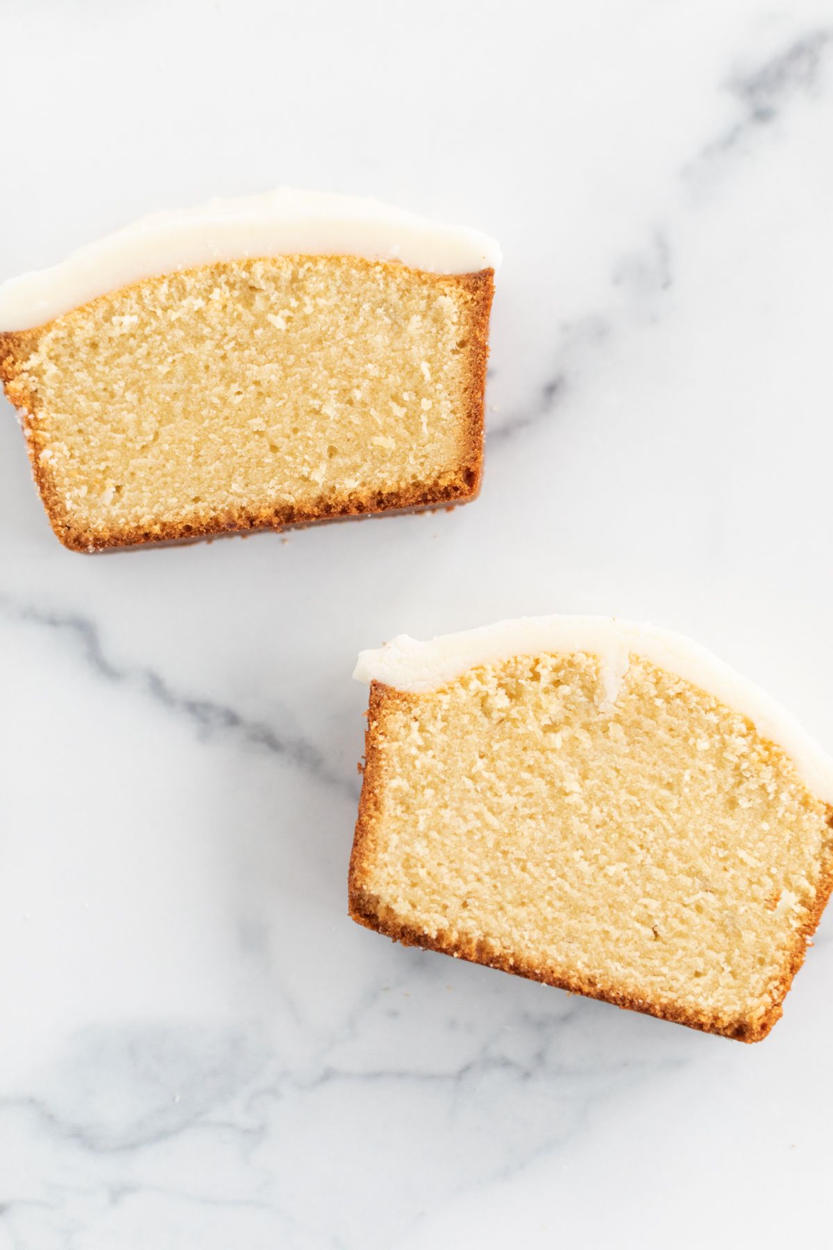 Two slices of an easy pound cake recipe with frosting on top, on a marble countertop.