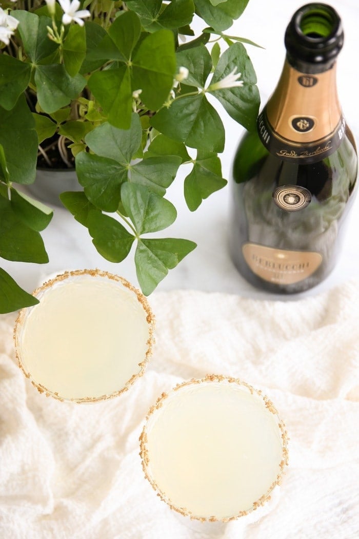Two gold St. Patrick's Day cocktails next to a bottle of champagne