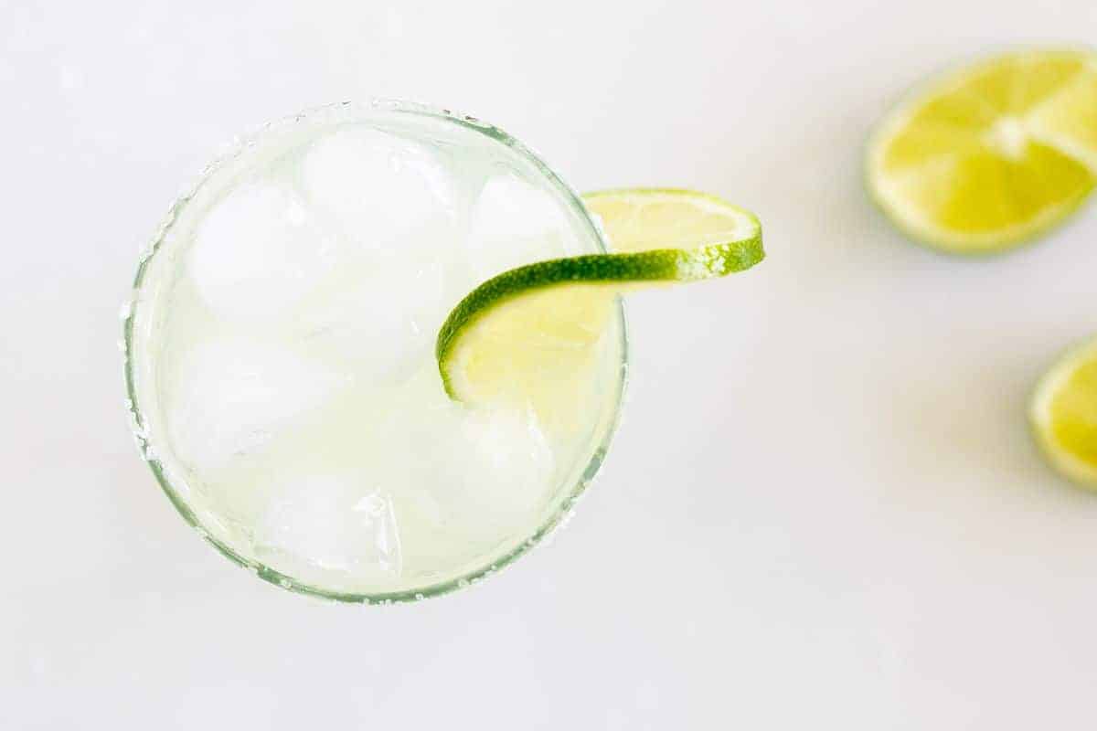 A clear glass with a homemade margarita, rimmed with salt and a slice of lime on a white background.